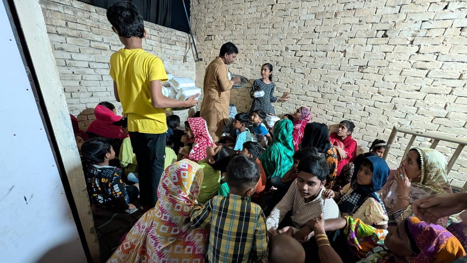 Impact City Church Arif Wala: volunteers carrying in meals to a packed room of families