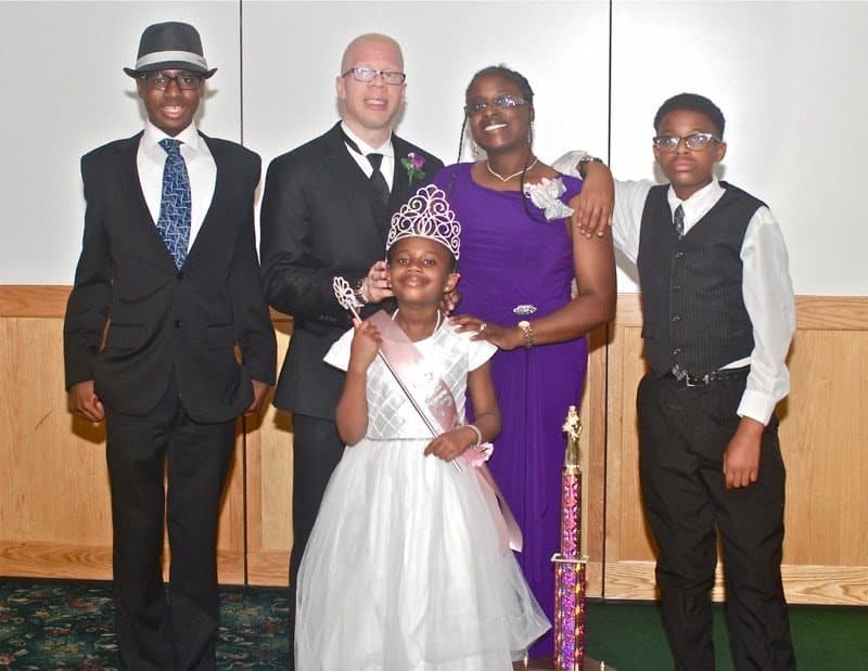 A crowned young lady in a white gown with her family