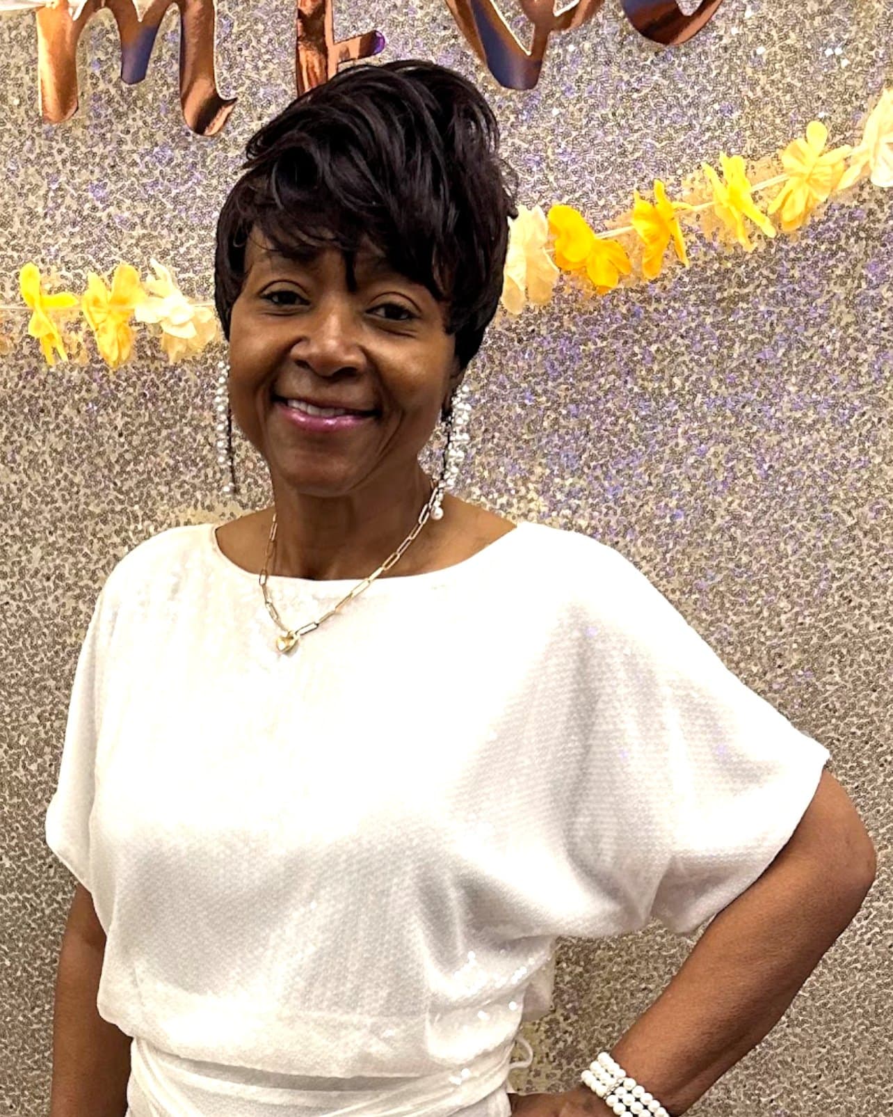 Elder Shira Dunson, Director of the I-Impress God Cotillion, in white before a sequined backdrop