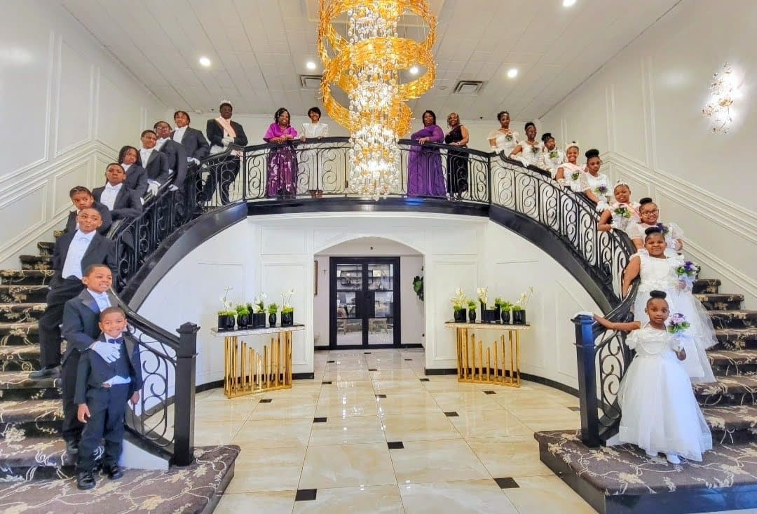 Young ladies in white gowns and young gentlemen in tuxedos posed along a grand double staircase