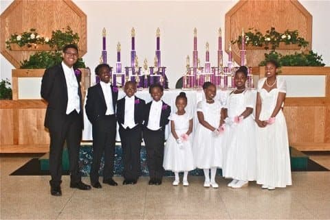 Young gentlemen in tuxedos and young ladies in white gowns standing in a row