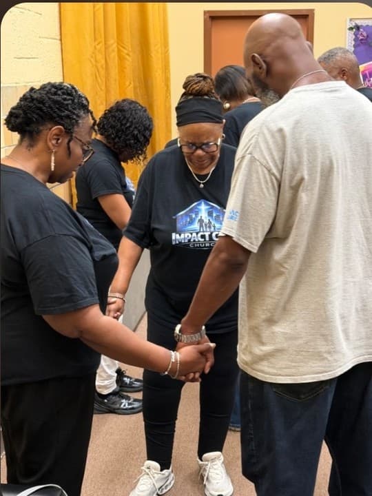 Impact City members praying together, hands joined