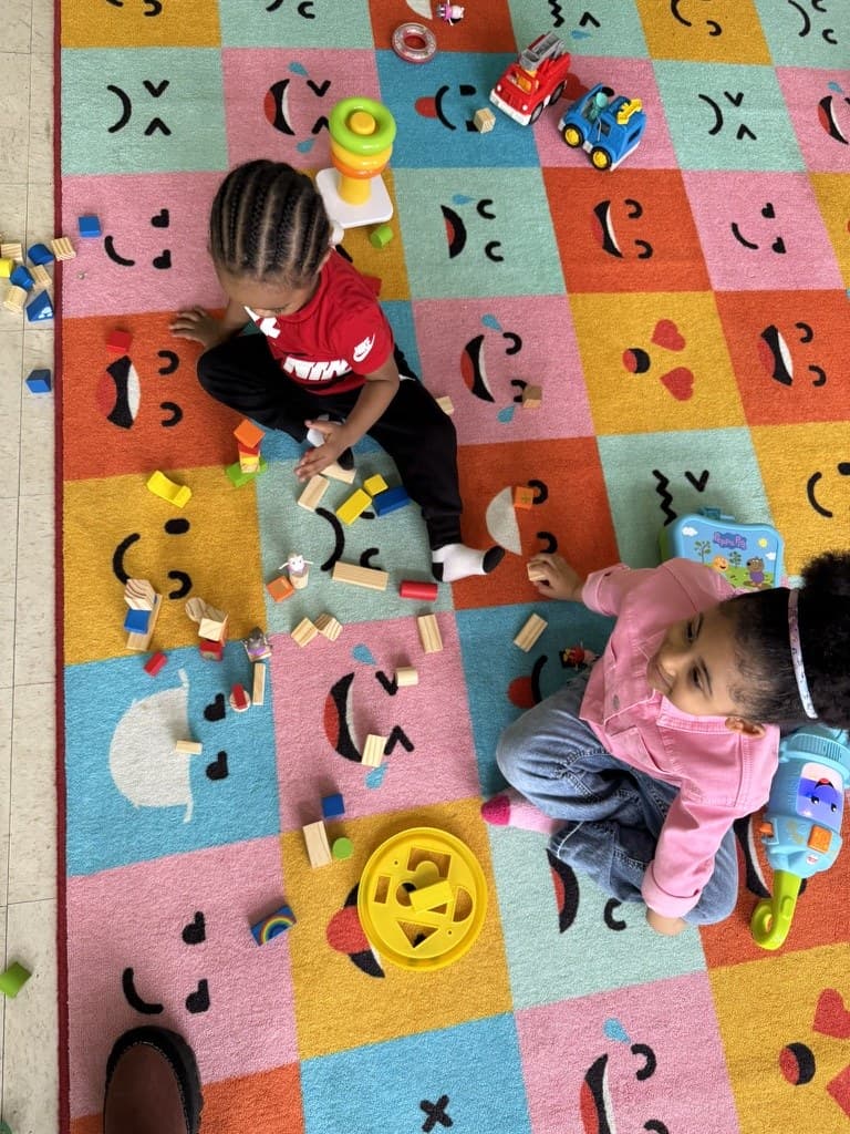 Two young children building with wooden blocks on the alphabet carpet