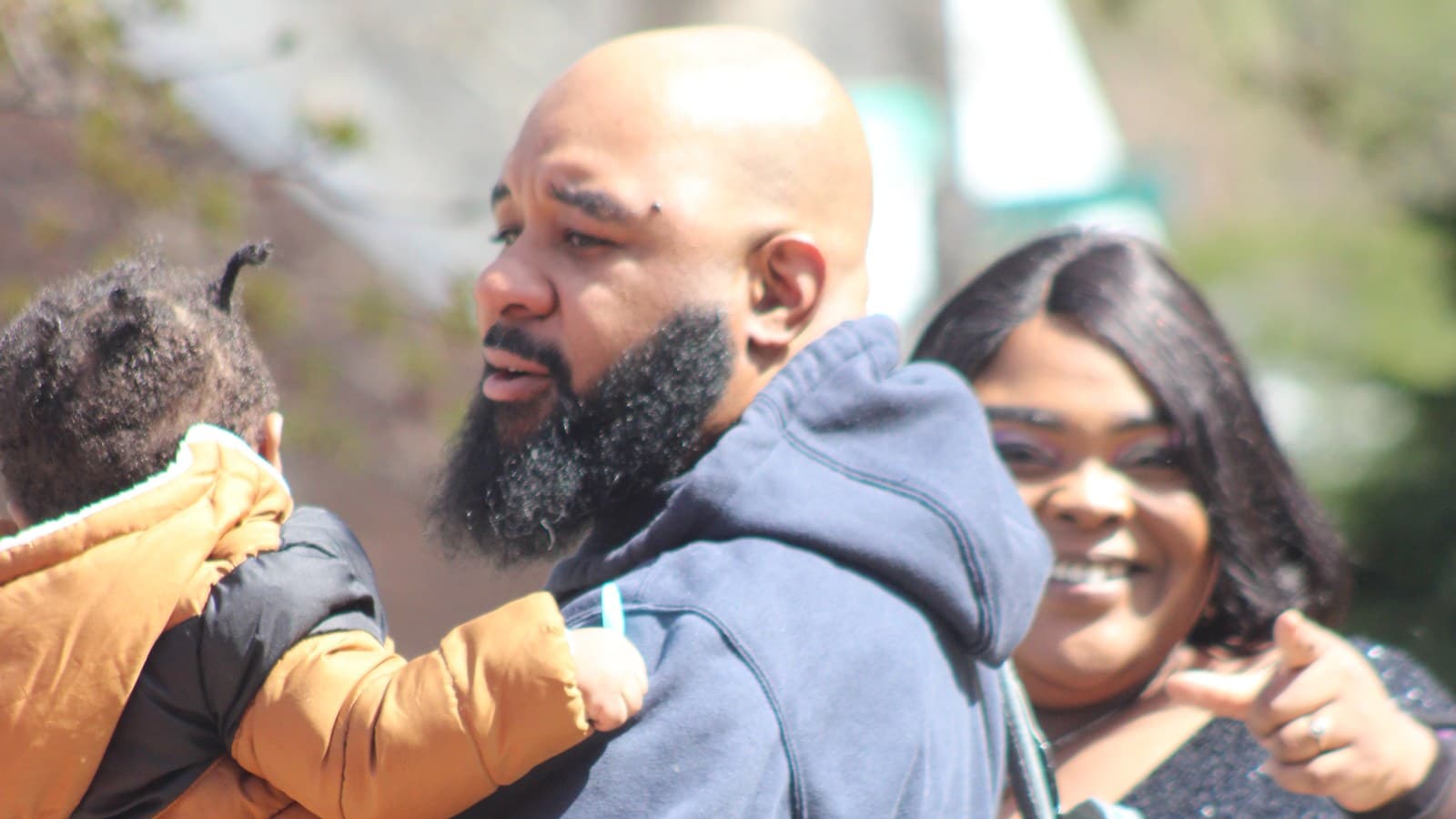 A father holding his toddler, mother beside them, outside on a Sunday